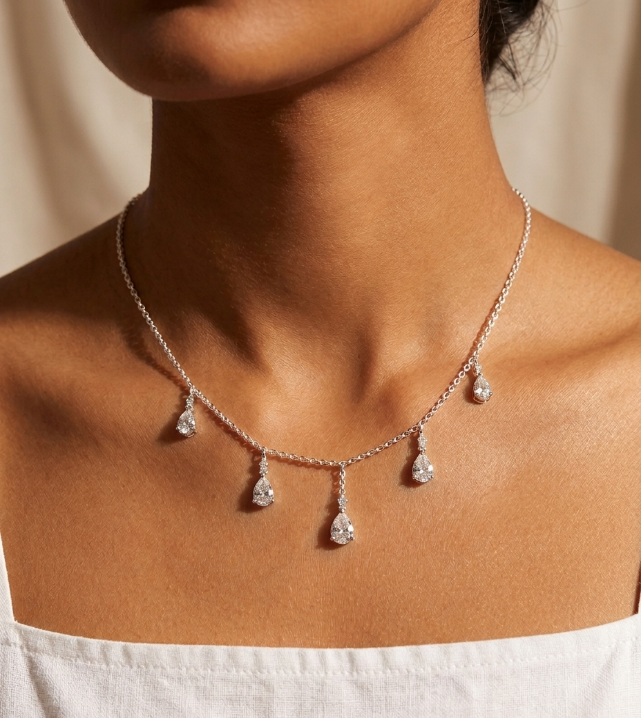 Necklace with teardrop-shaped pendants on a person wearing a white top against a beige background