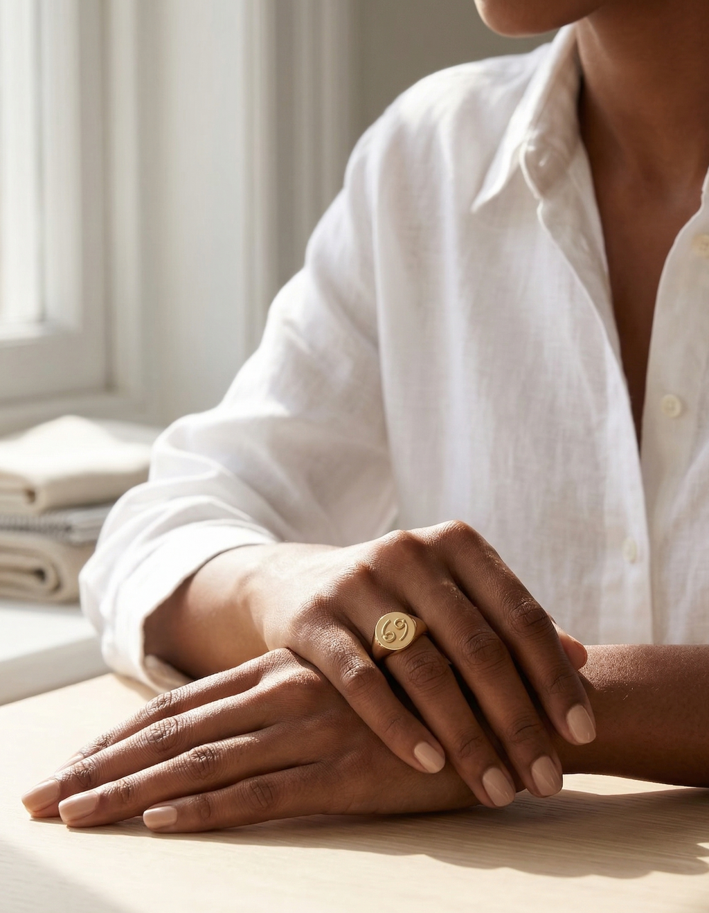 Person wearing a gold ring on a light surface with a neutral background
