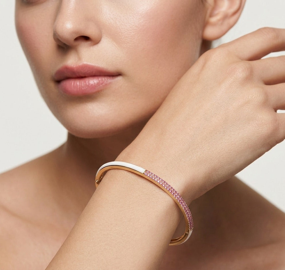 Close-up of a woman's hand wearing a rose gold bracelet with pink stones on a neutral background