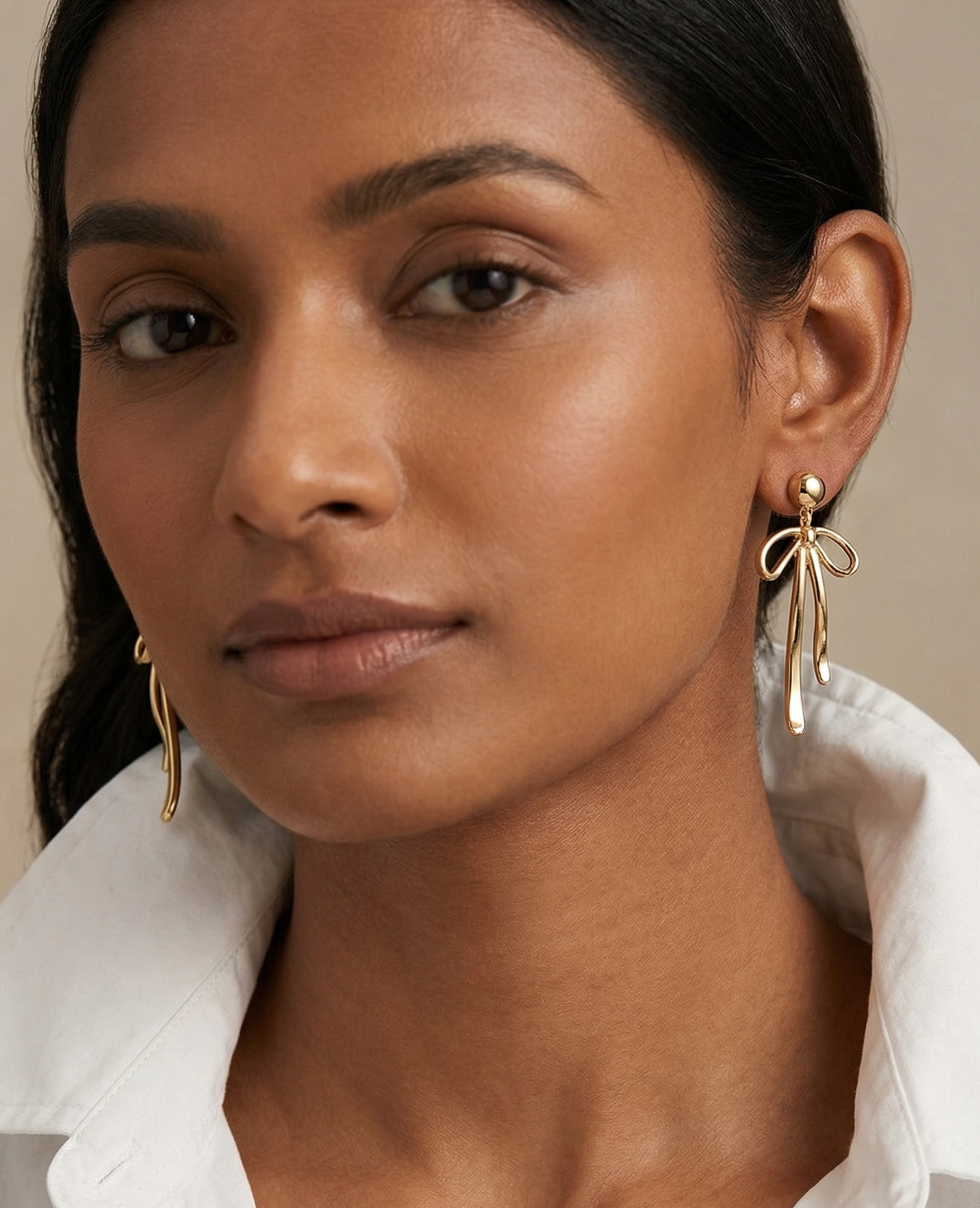 Woman wearing gold earrings with a neutral background