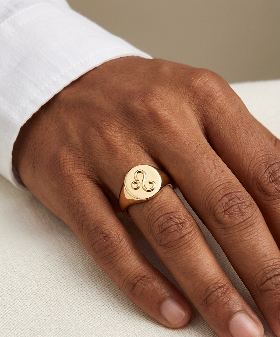 Gold ring with a heart design on a person's finger against a neutral background