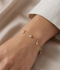 Gold bracelet with star and heart charms on a wrist against a neutral background