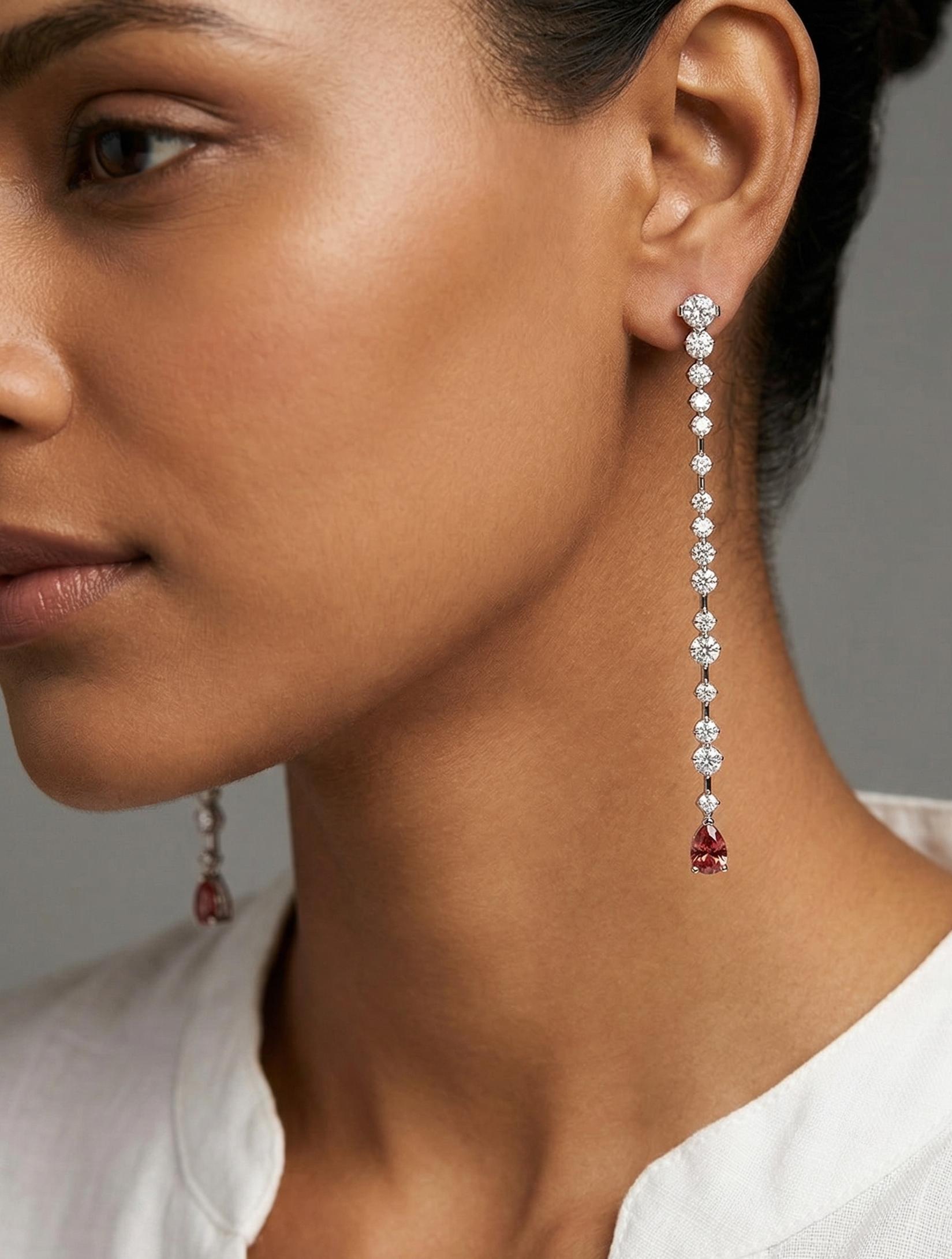 Close-up of a woman wearing diamond earrings with red gemstones on a neutral background