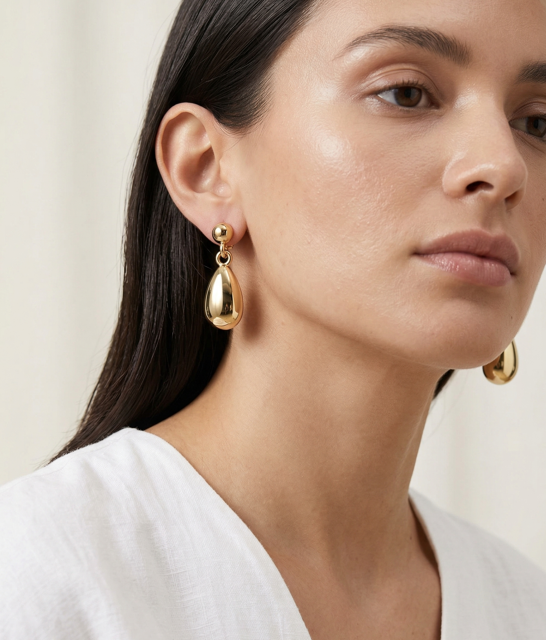 Woman wearing gold teardrop earrings against a neutral background
