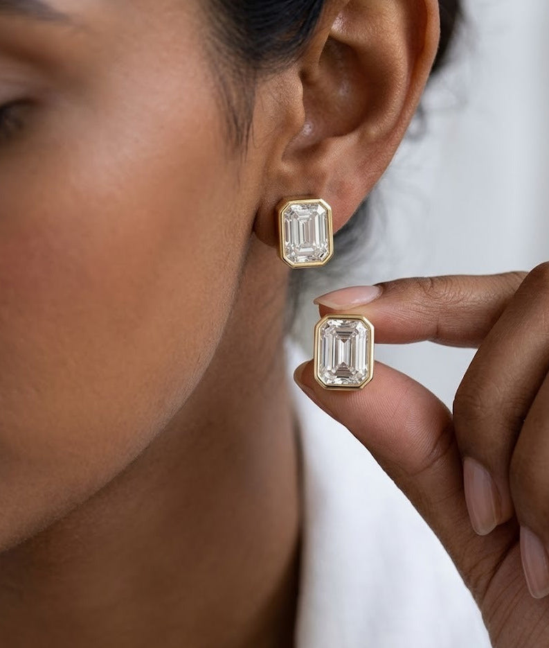 Close-up of a person wearing gold earrings with a hand holding one, against a neutral background.