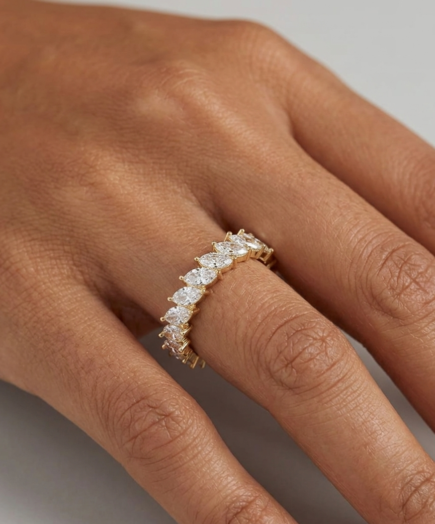 Gold ring with diamonds on a person's finger against a neutral background