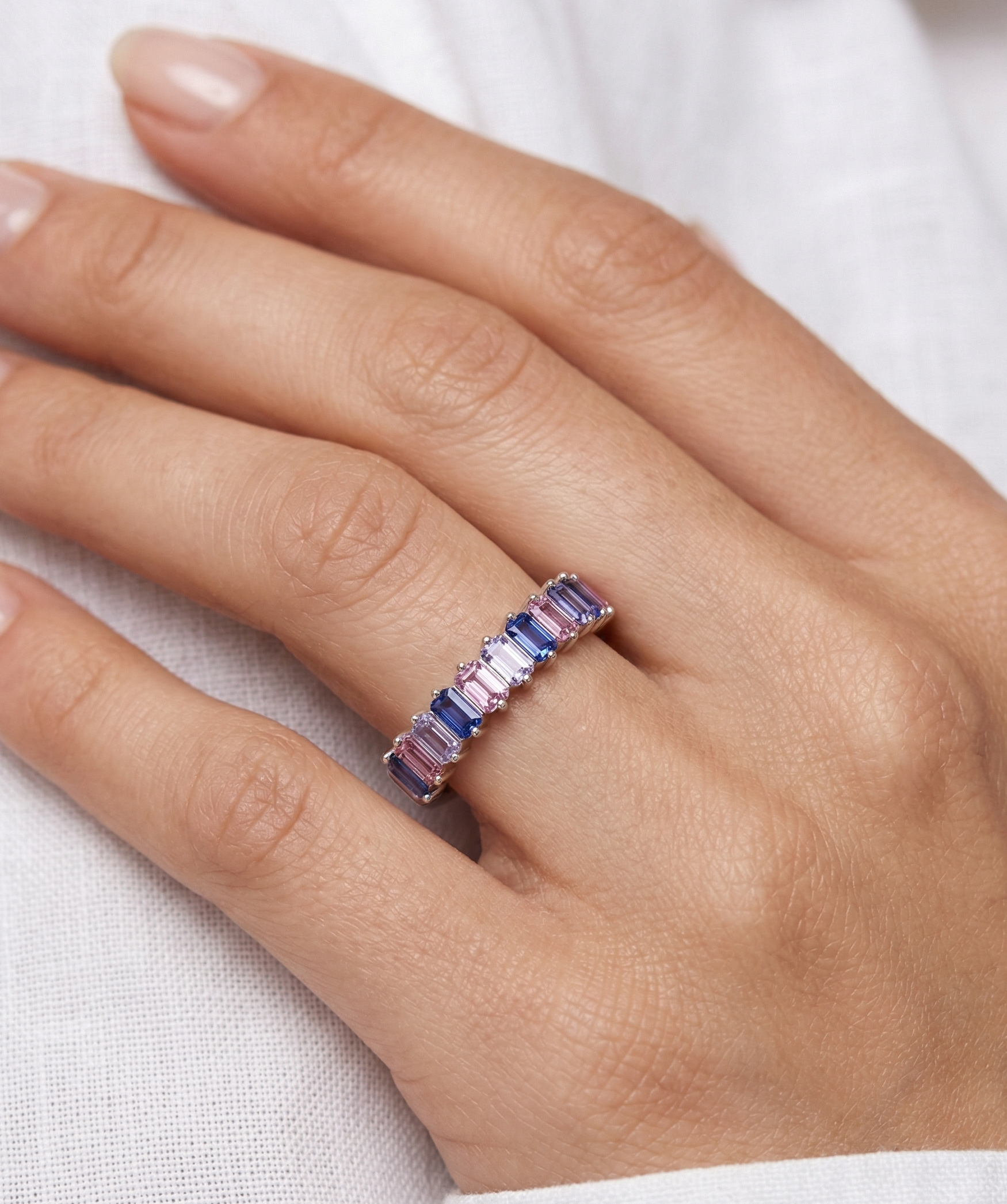 Hand wearing a ring with pink and blue gemstones on a white background