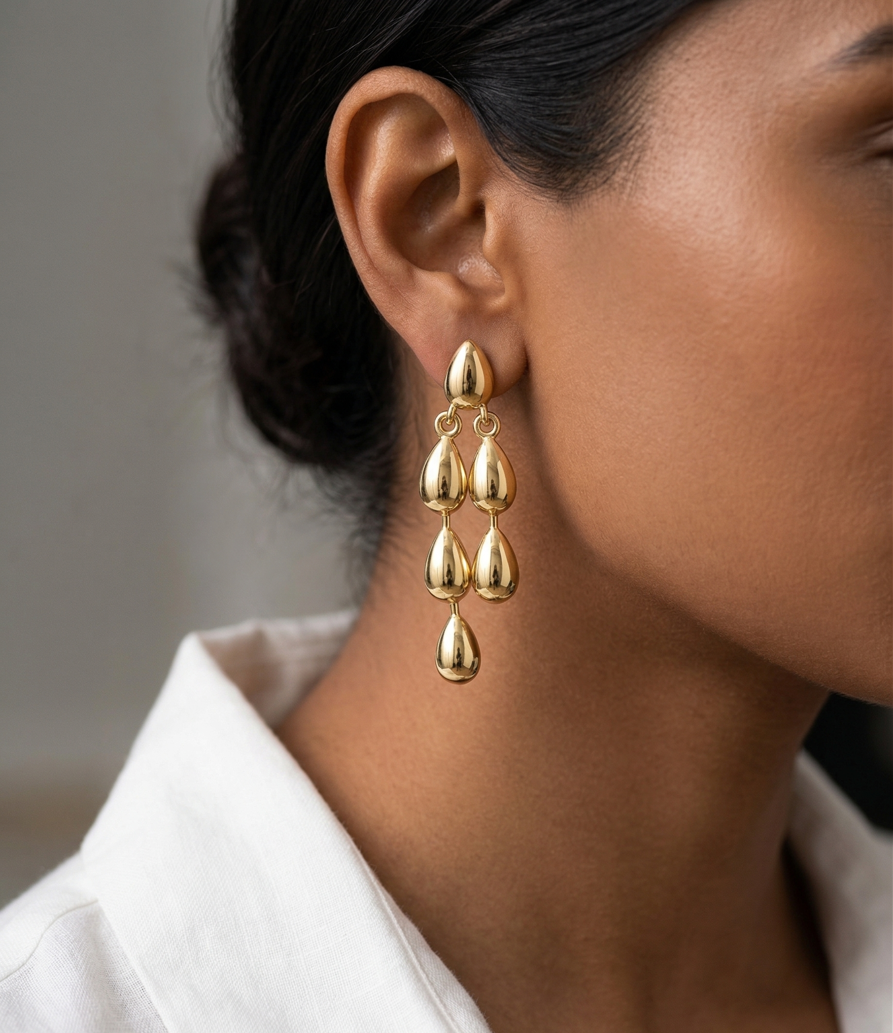 Gold teardrop earrings worn by a person with a neutral background