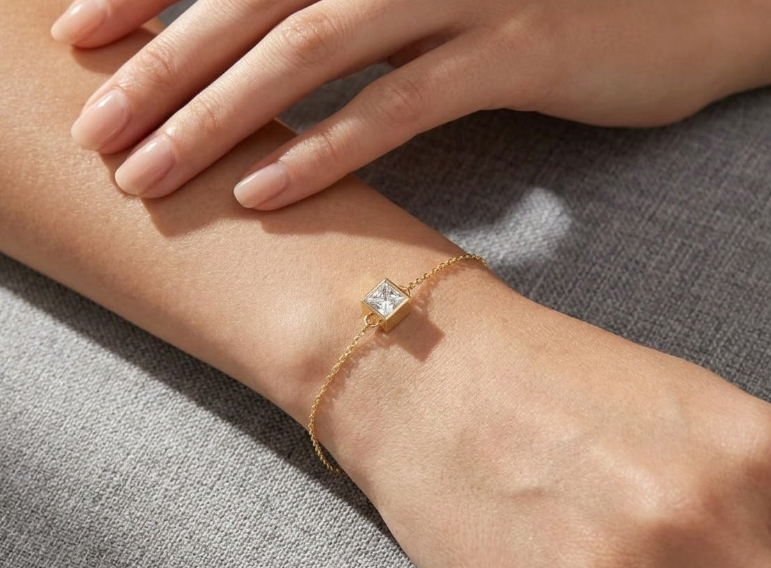 Gold bracelet with a diamond on a wrist against a gray background