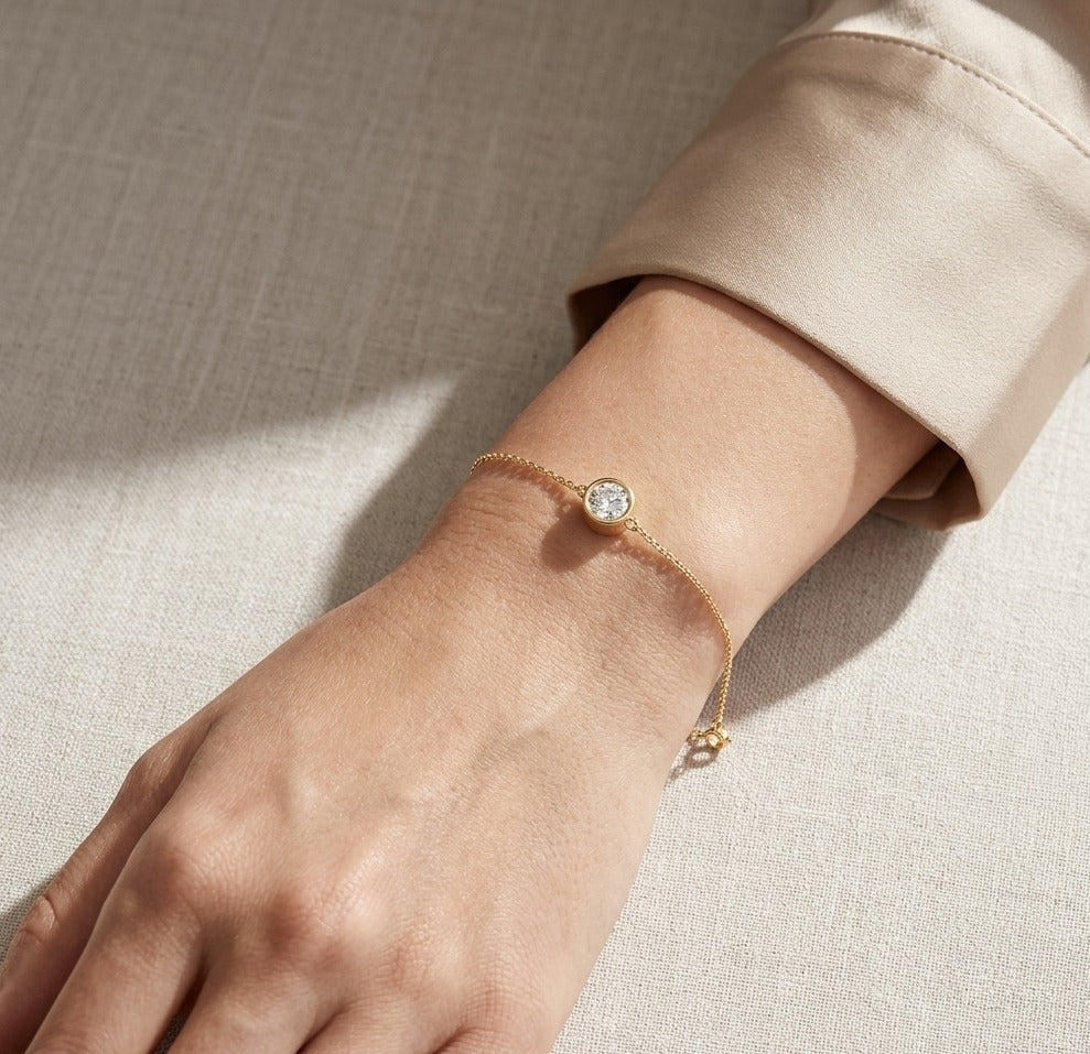 Gold bracelet with a diamond on a wrist against a neutral background