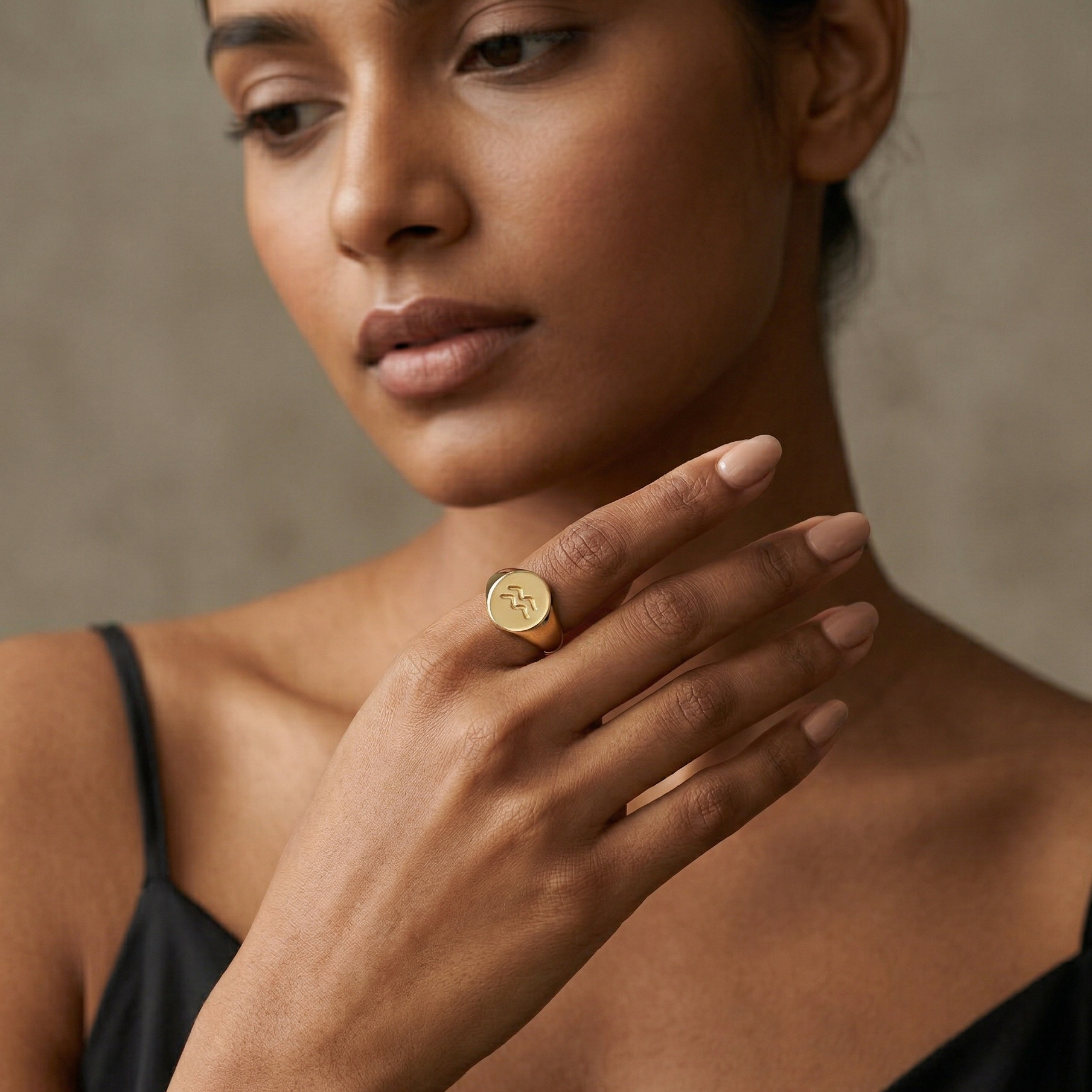 Woman wearing a gold ring on her finger against a neutral background