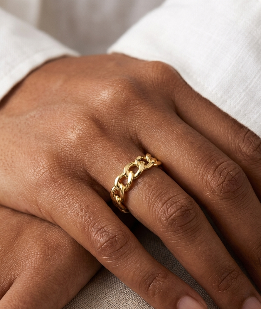 Gold chain ring on a person's finger with a neutral background