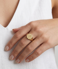 Gold ring with a heart design on a person's finger against a white background
