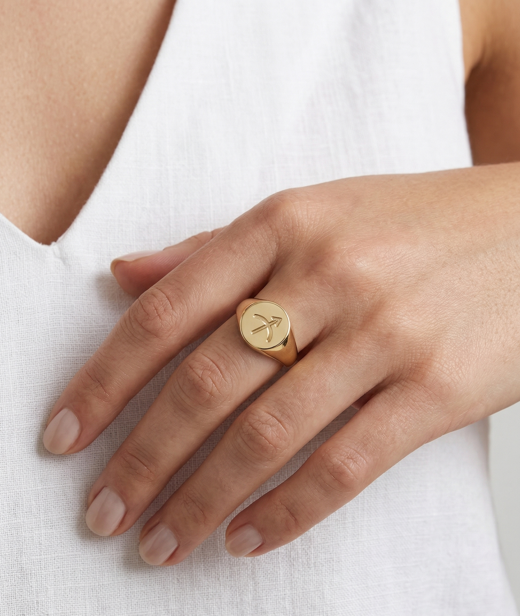 Gold ring with a heart design on a person's finger against a white background